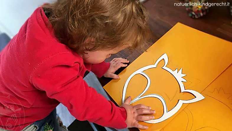 Mädchen paust die Vorlage für die Fuchslaterne auf orangefarbenen Karton